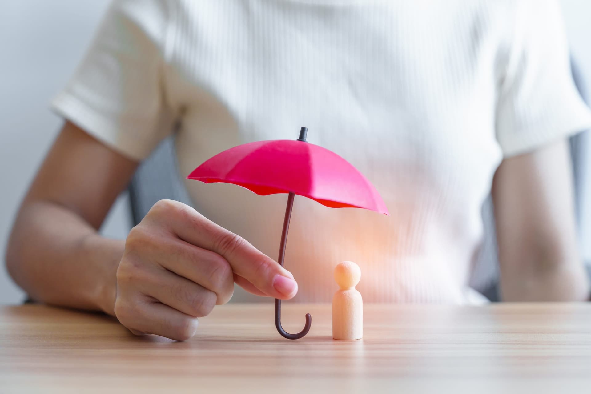 Hand holding a small red umbrella over a wooden figure, symbolizing insurance protection for ABA therapy coverage