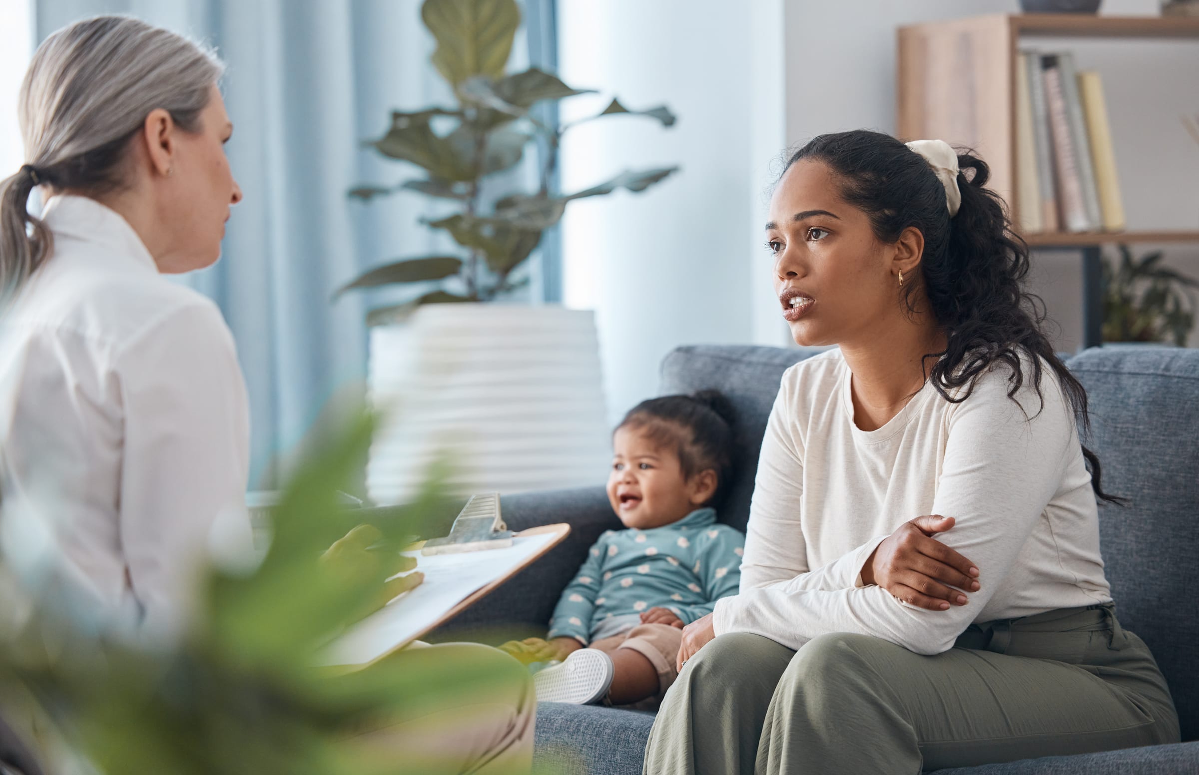 BCBA clinician consulting with a mother and her infant, reviewing documentation on a clipboard during a behavior consultation session