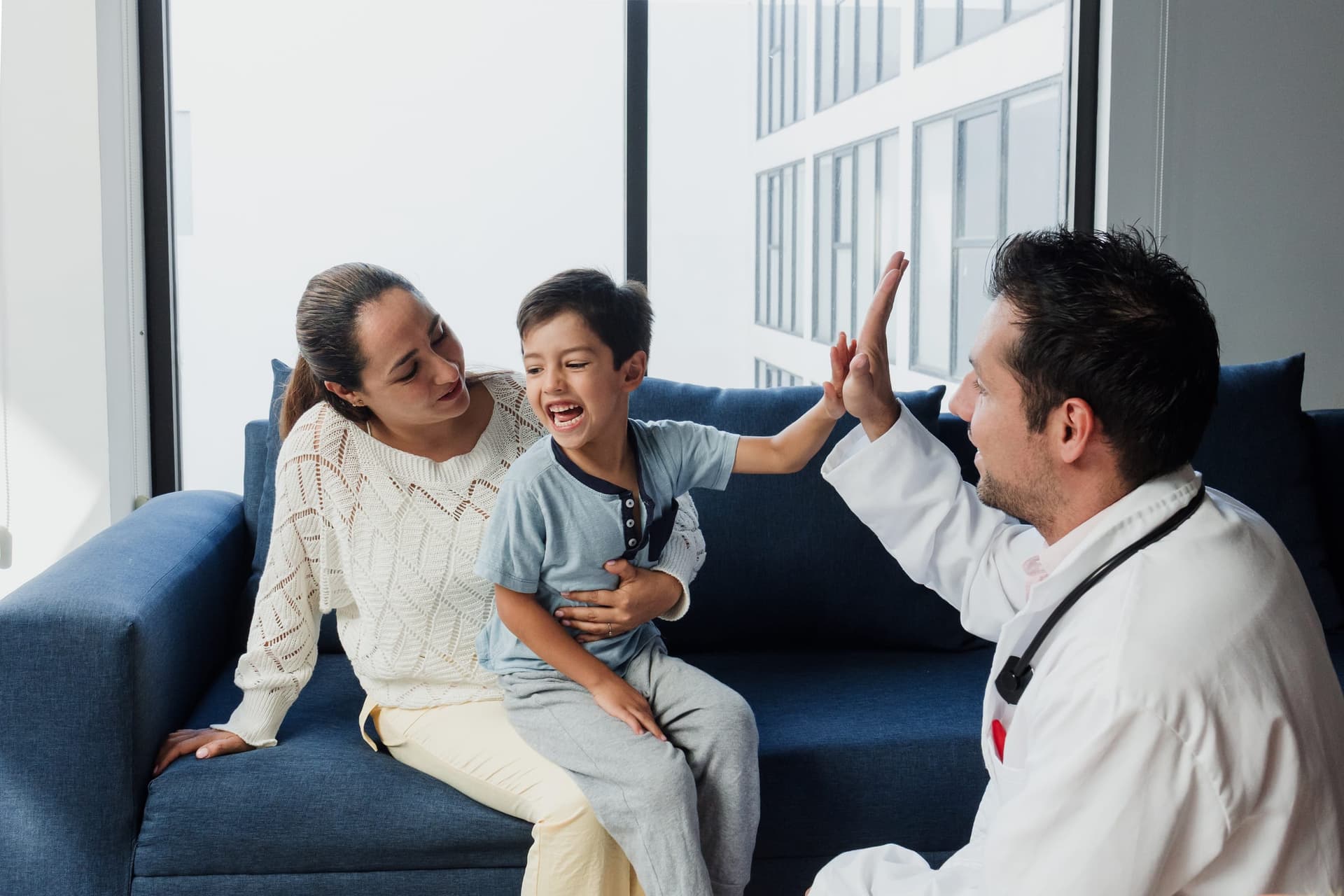 Young boy happily high-fiving his pediatrician during a checkup visit with his mother