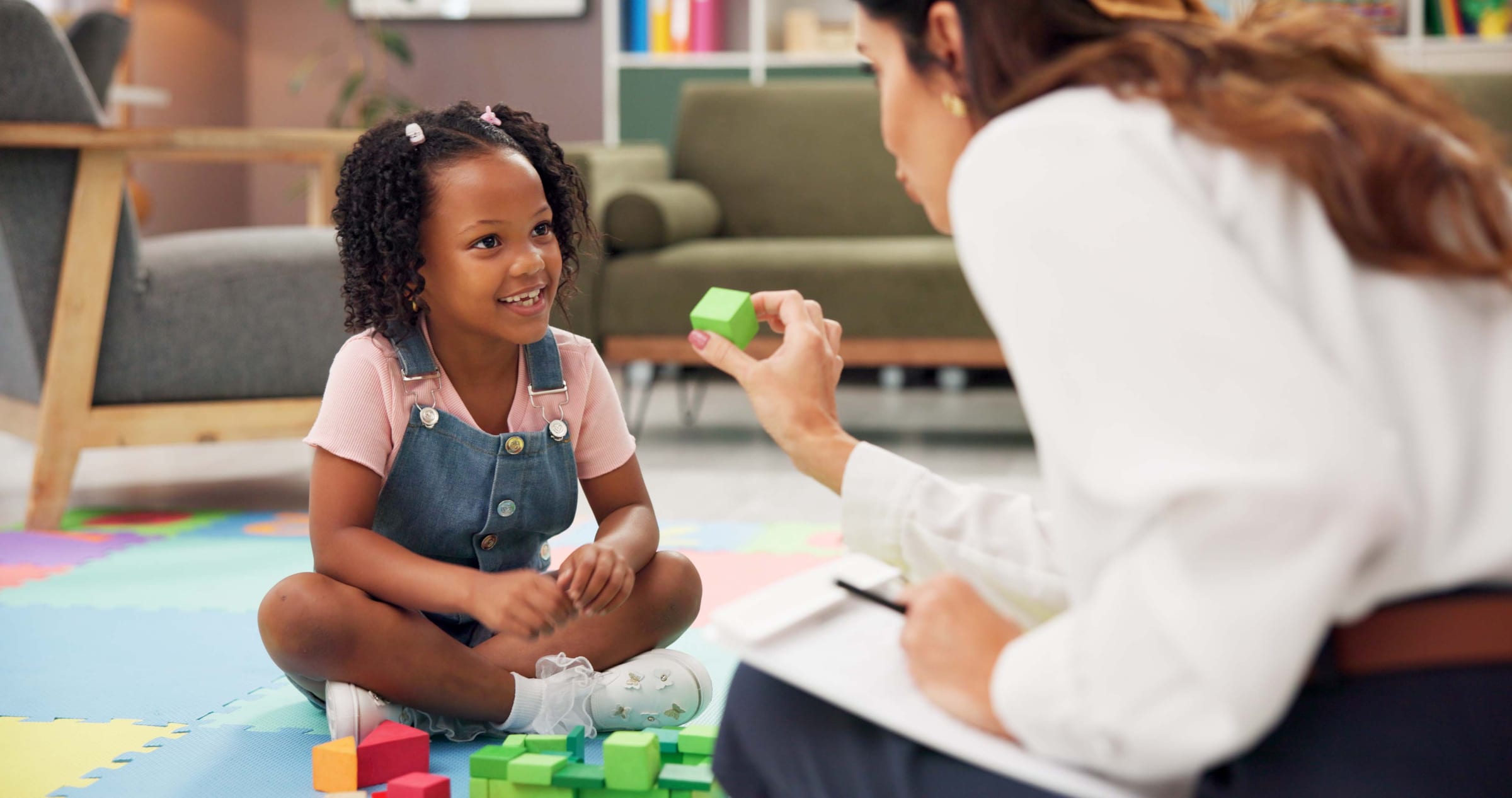 Registered behavior technician conducting an in-home ABA therapy session with a young girl, holding a block while the child smiles during a discrete trial