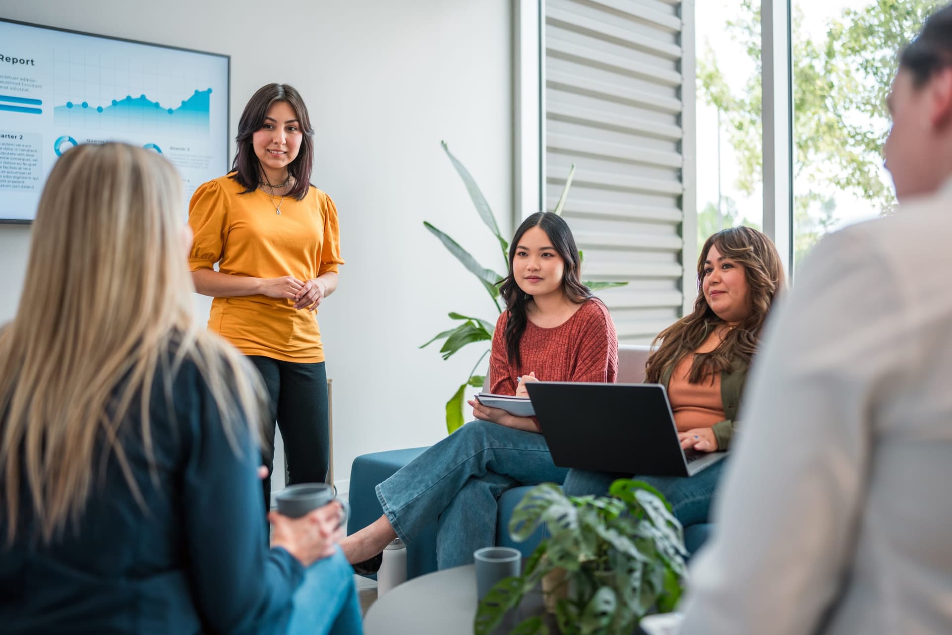 A behavior analyst presents clinical data on a screen to a diverse team of colleagues in a modern collaborative workspace during a program review meeting